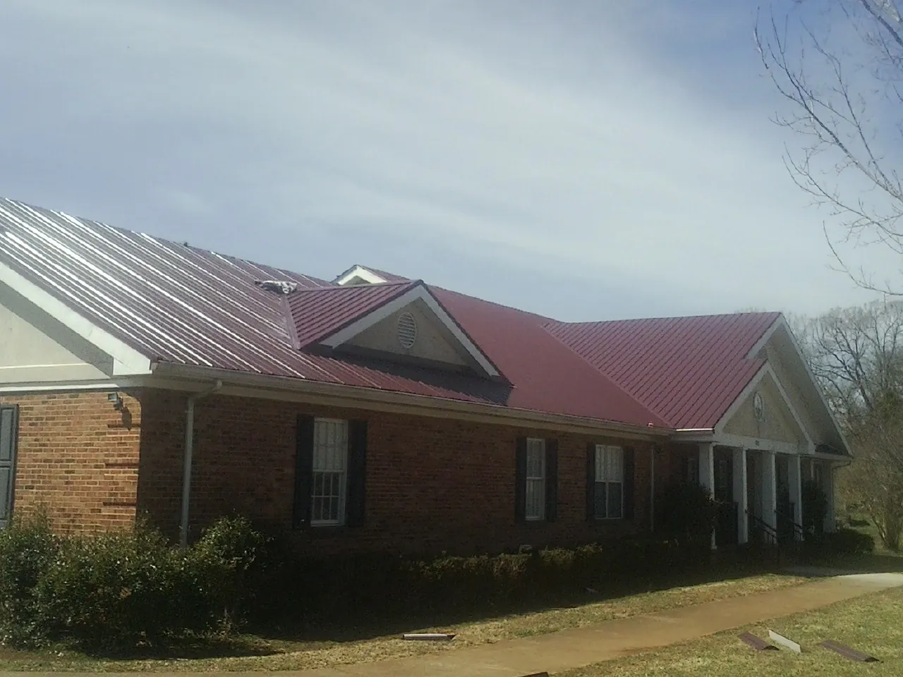 Red metal roof with gabled entries on a long brick building, from a Hail Damage Roof Repair job in Sun City West