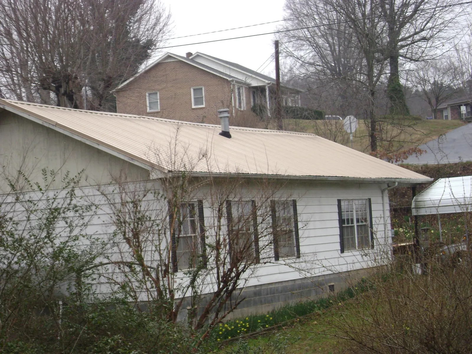 Tan metal roof on a white sided house set into a hillside — Commercial Roofing by Roofing Brothers in Sun City West
